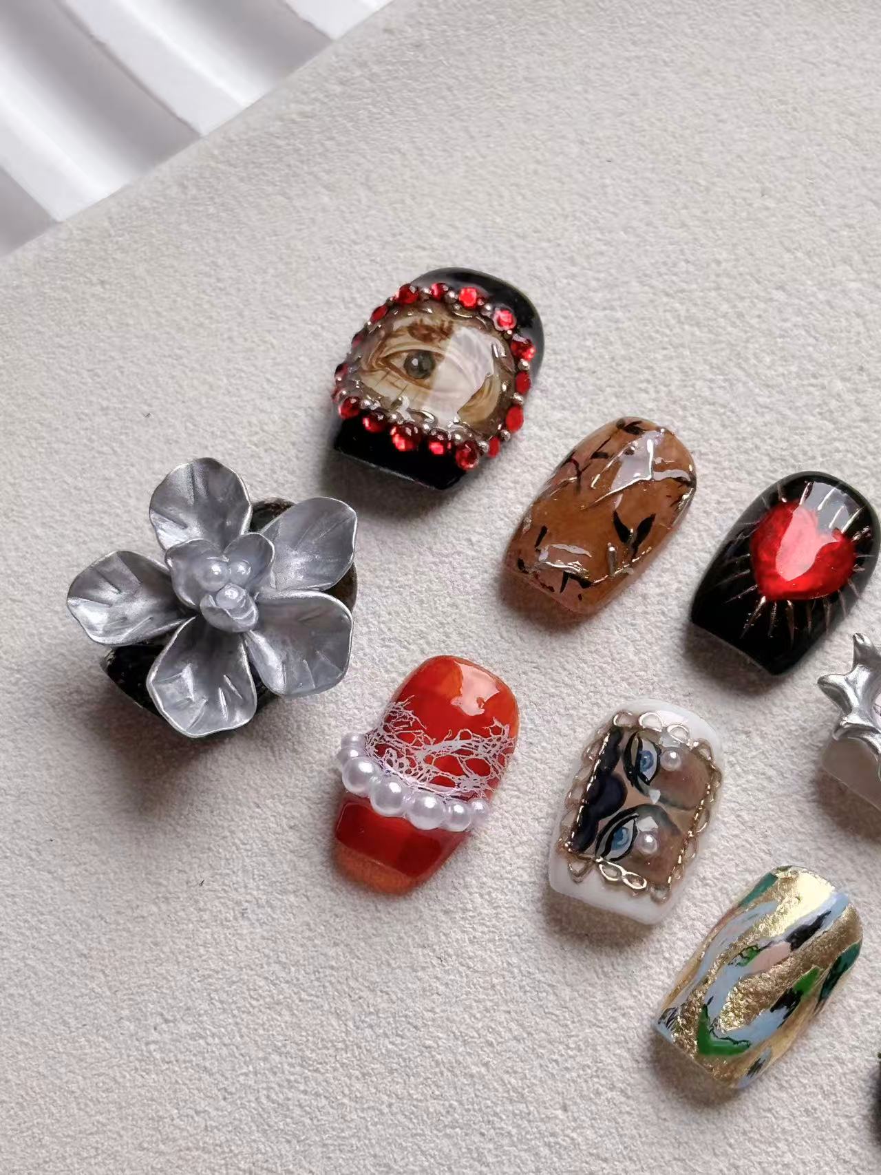 Close-up of artisan nail art showing a red 3D sacred heart and detailed eye motif with red rhinestones