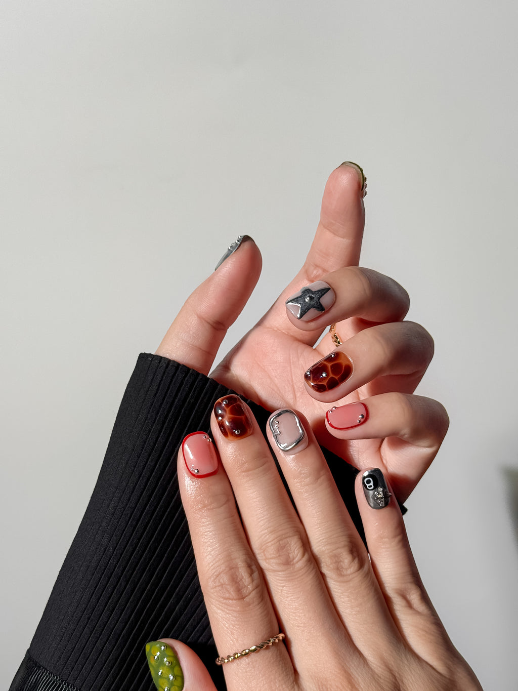 A full manicure display featuring a silver charm nail, moss green textured art, and tortoiseshell patterns for a trendy indie aesthetic.