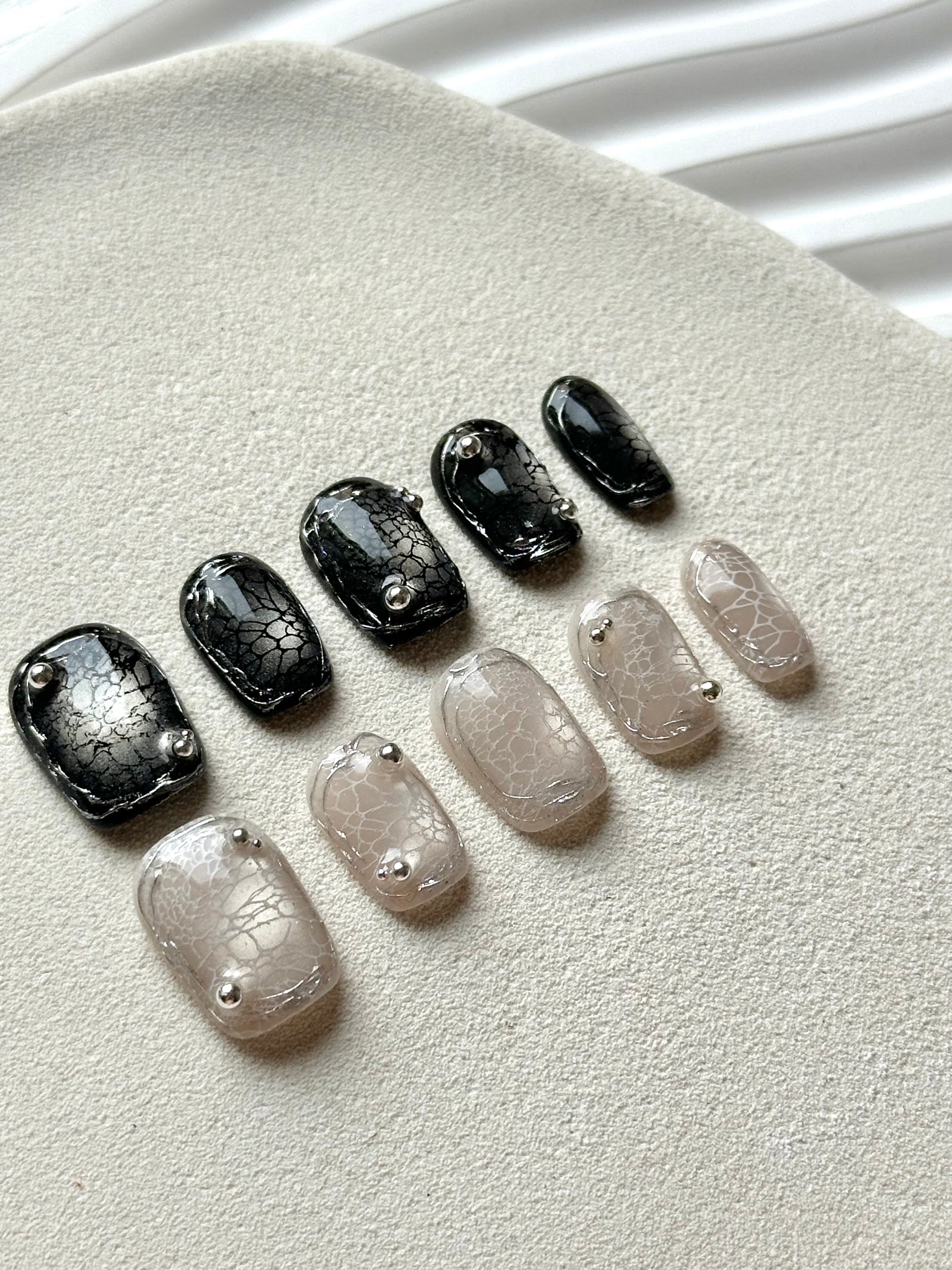 Angled view of edgy press-on nails with silver metallic accents and a high-gloss spider web pattern.