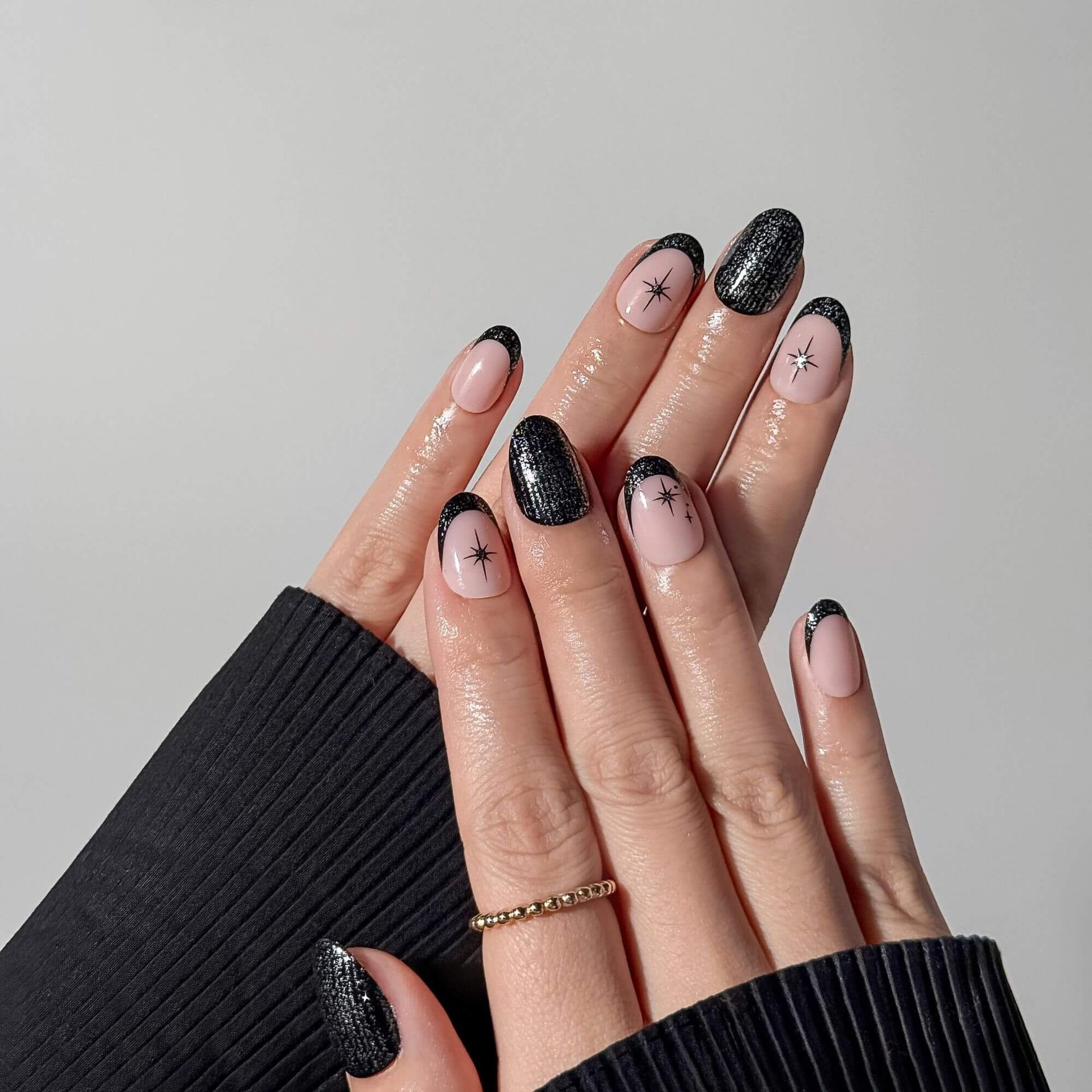 Hand wearing short round black glitter French tip nails with hand-painted starburst motifs