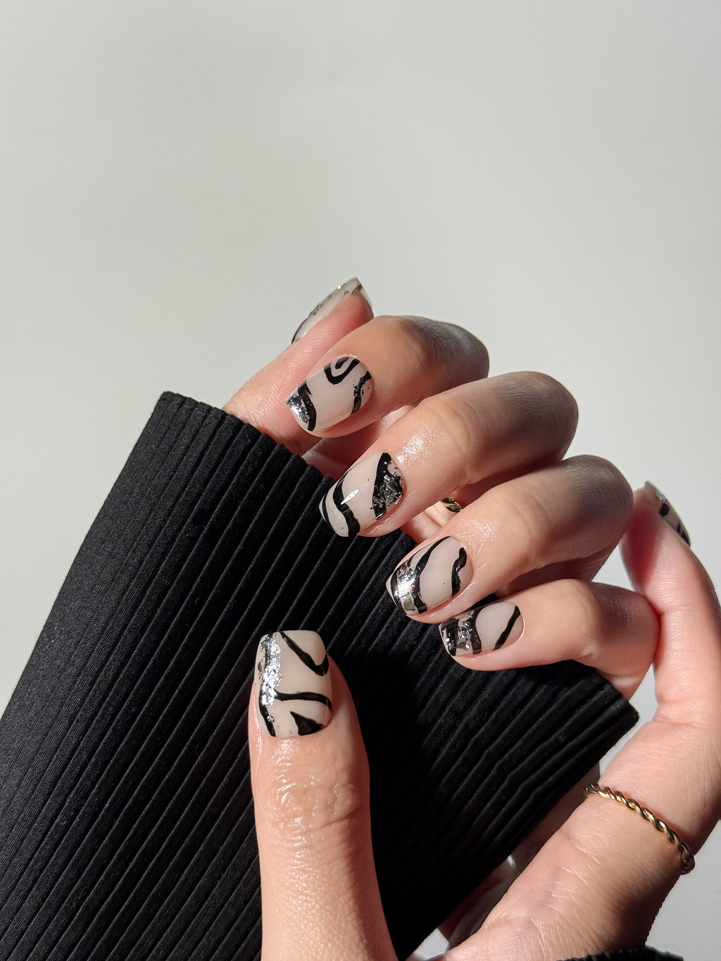 Close-up of an animal print manicure with silver foil details, styled with a black ribbed sweater. Short square press-on nails that are handmade and reusable.