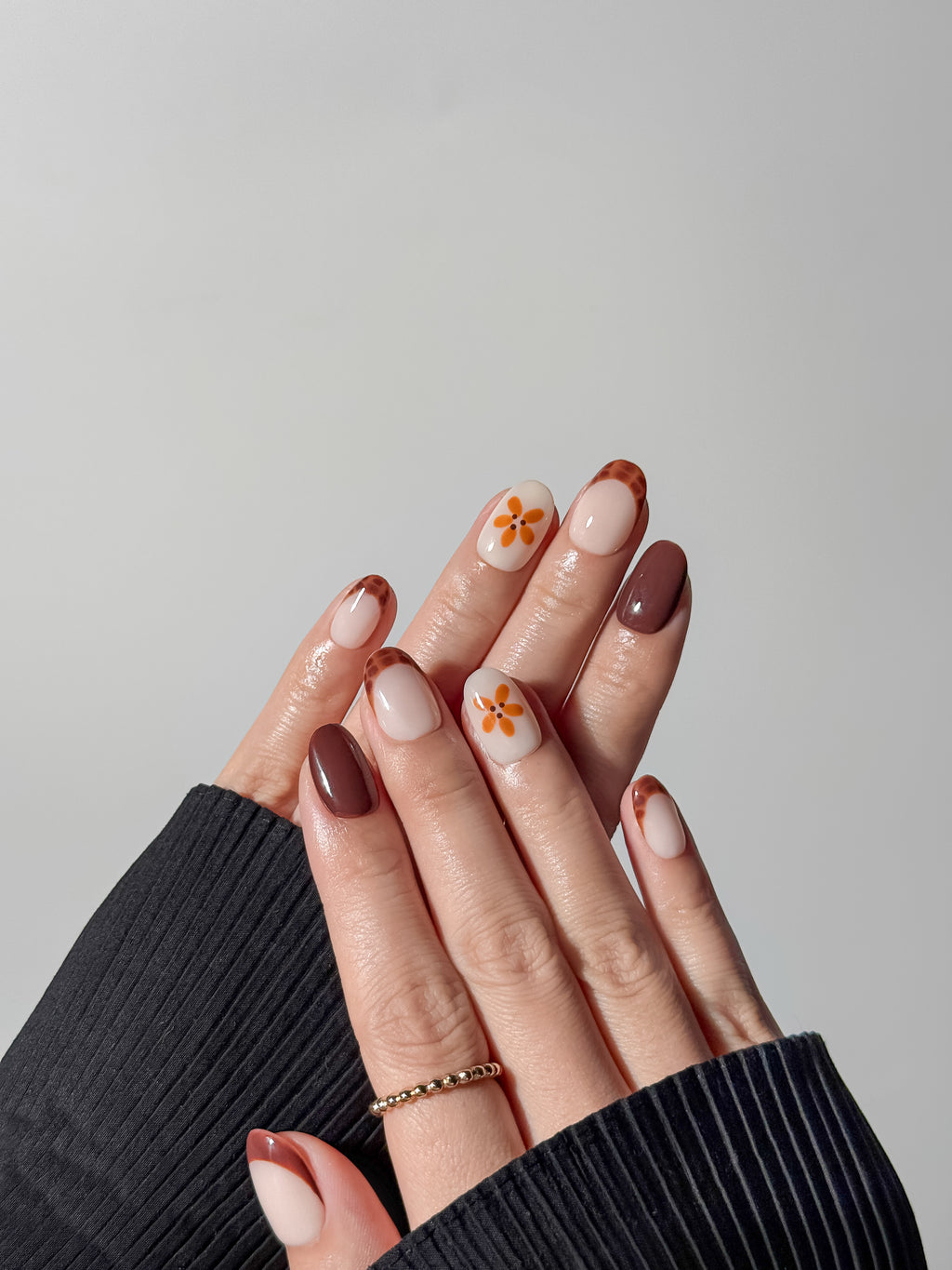 Hand model wearing short round mocha brown nails with amber flower accents and tortoise shell French tips.