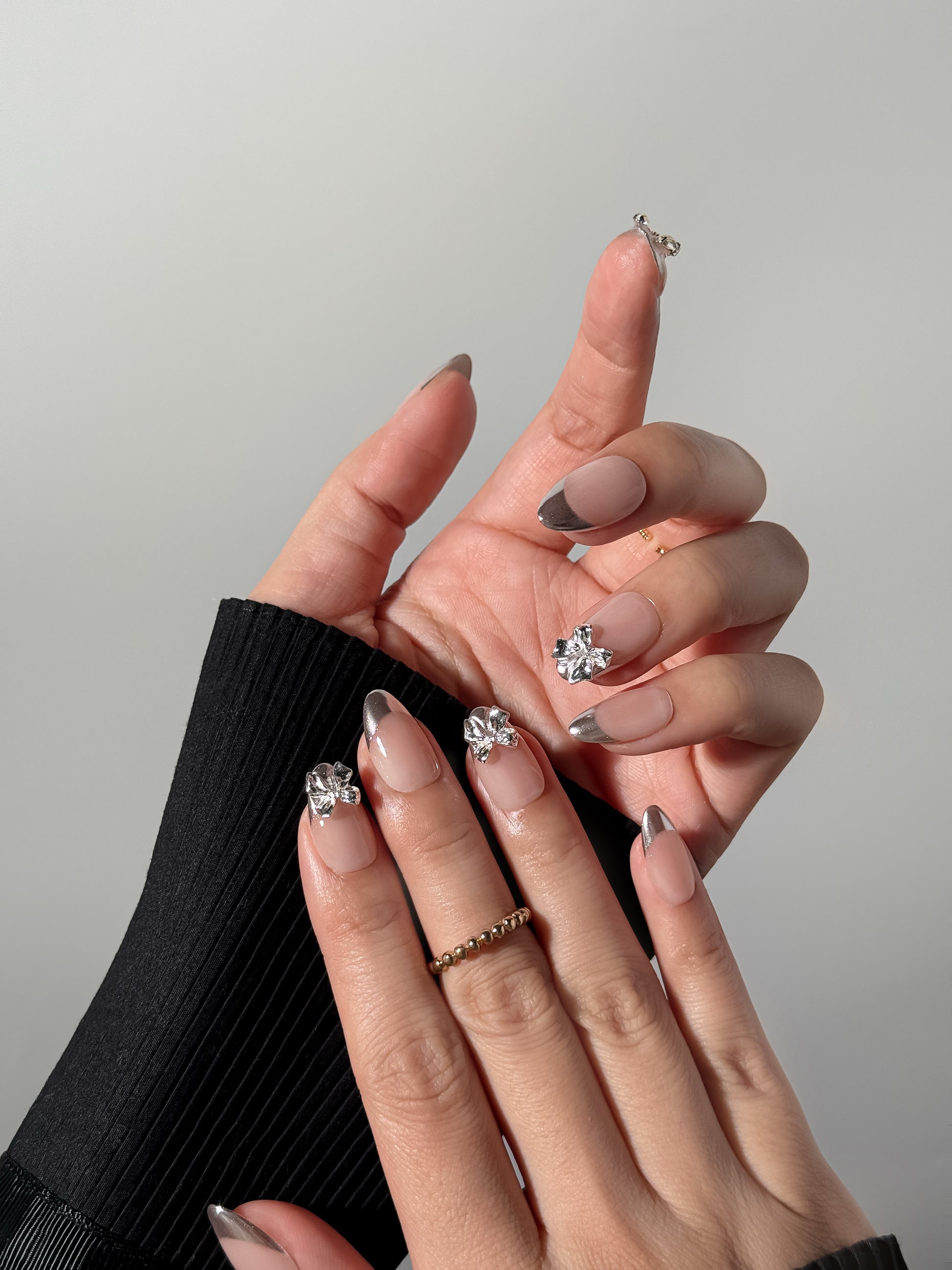 Elegant clean girl press-on nails worn on hand featuring soft nude color, silver tips and glossy 3D bow accents, modern reusable press-on nails.