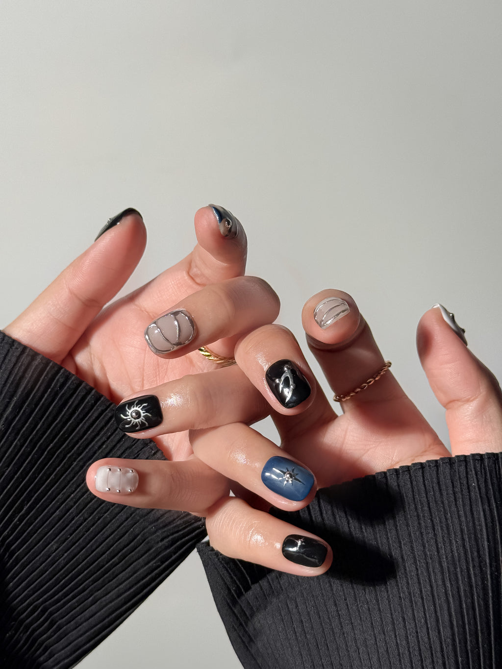 Both hands displaying a dark, celestial nail art design. The look features a mix of matte and glossy finishes, 3D silver star charms, metallic studs, and a deep blue accent nail with a silver North Star motif