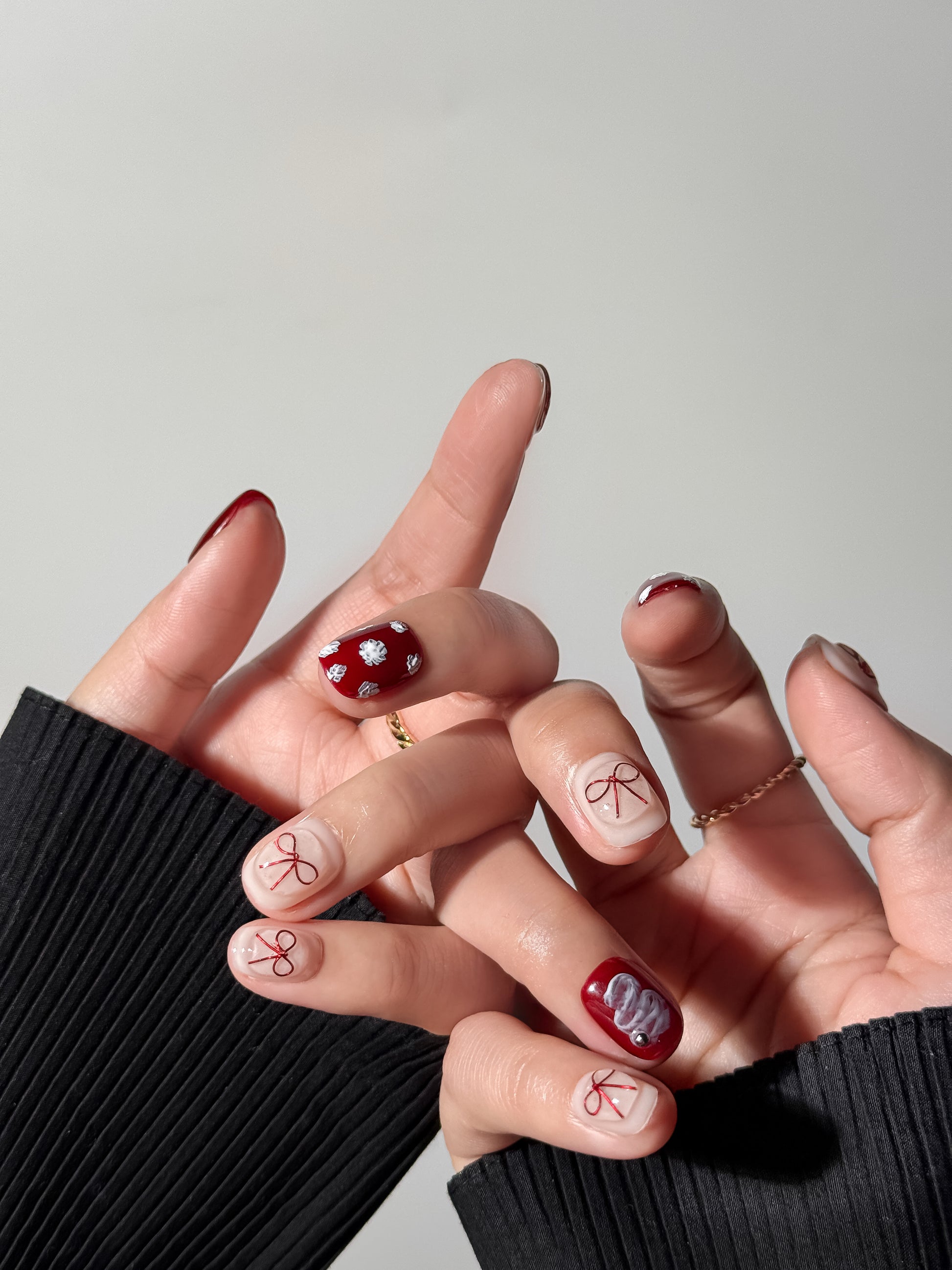 lifestyle shot of hands showcasing a feminine red and nude manicure with dainty hand-painted ribbons and different textures.