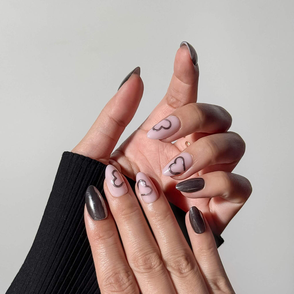 Hand wearing almond-shaped gunmetal silver chrome press-on nails mixed with blush pink nails featuring silver heart outlines.