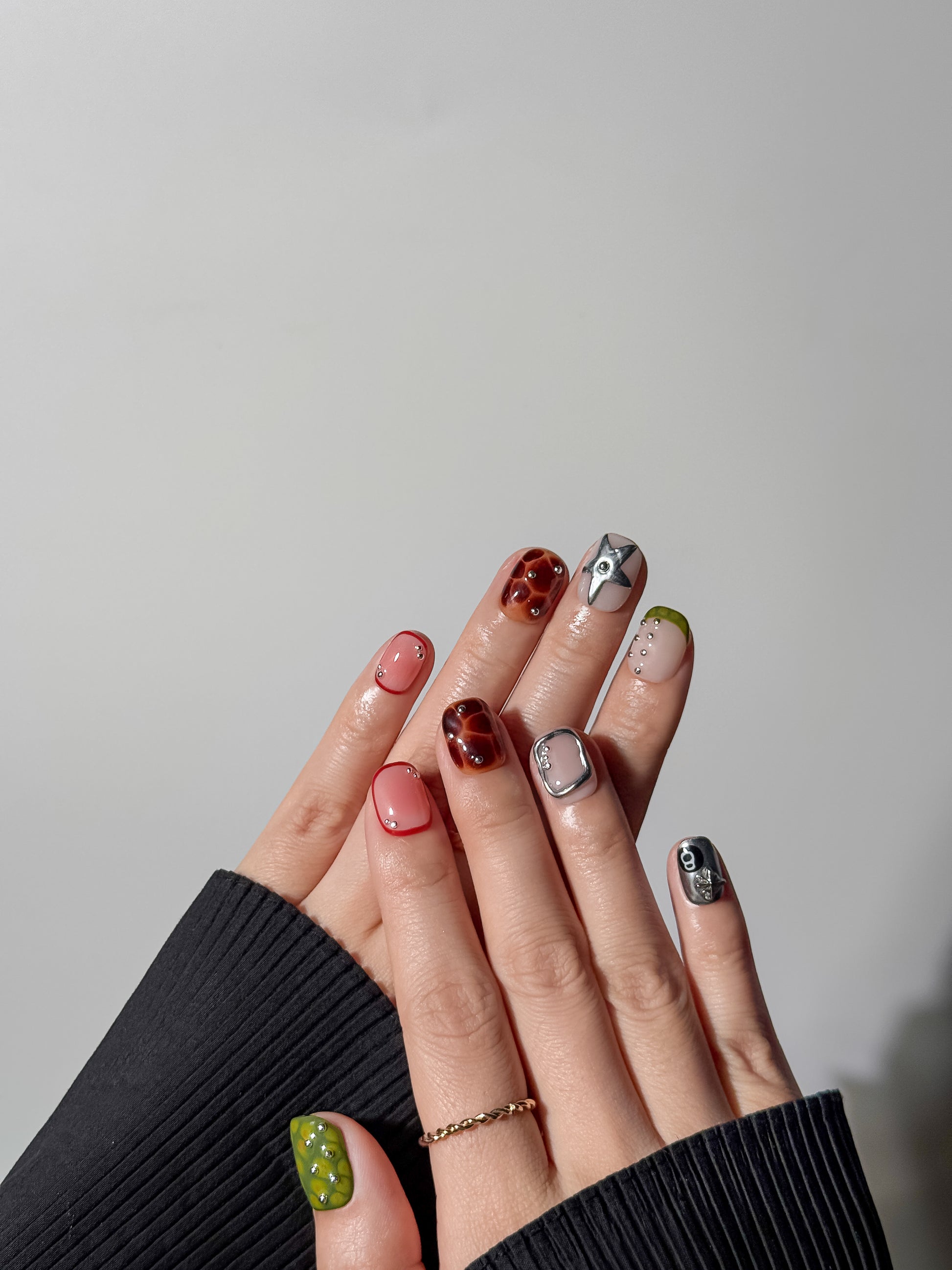 hand showcasing a detailed manicure with a large 3D silver star on the middle finger, surrounded by tortoiseshell, silver chrome, and red-rimmed jelly nails.