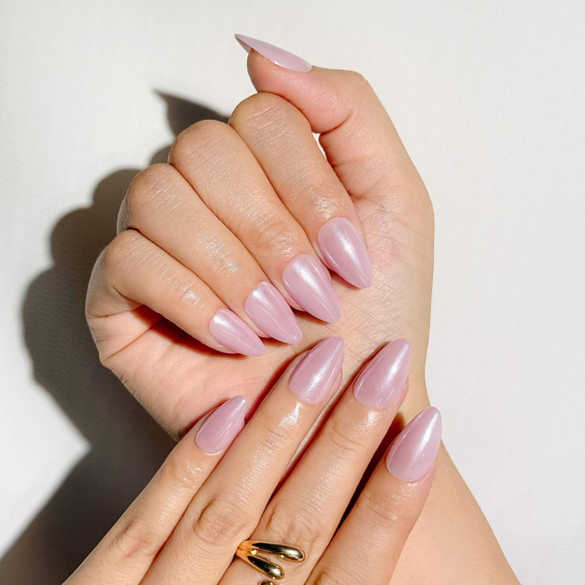 Nahaufnahme einer Hand mit eleganten babyrosa Nägeln in Mandelform mit perligem Chrom-Glanz, kombiniert mit einem goldenen Statement-Ring für einen Braut-Look.