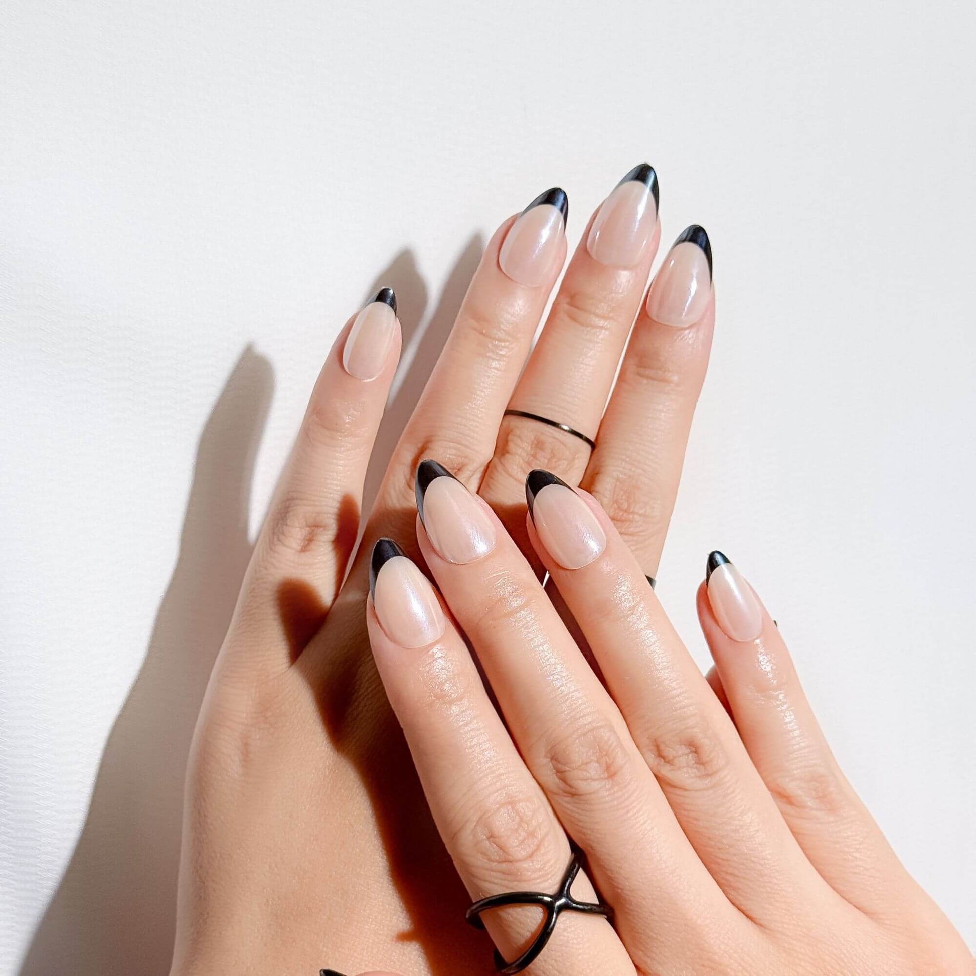 Lifestyle-Aufnahme einer Hand mit Justmee schwarzen French Tip Nägeln in Mandelform, die den verlängernden Effekt und das professionelle Salon-Finish zeigt.