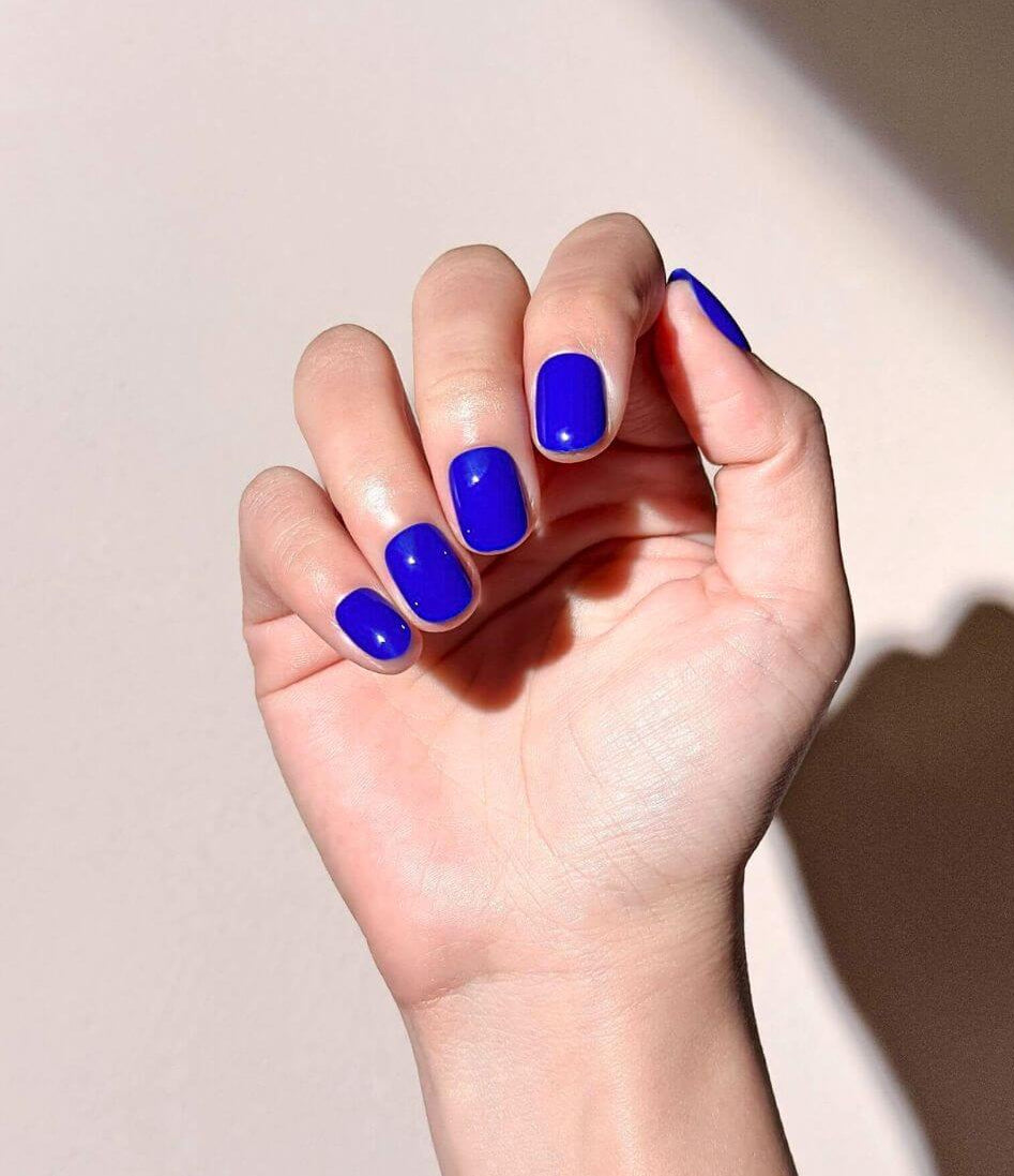 A hand wearing cobalt blue short press on nails in square shape with warm natural light