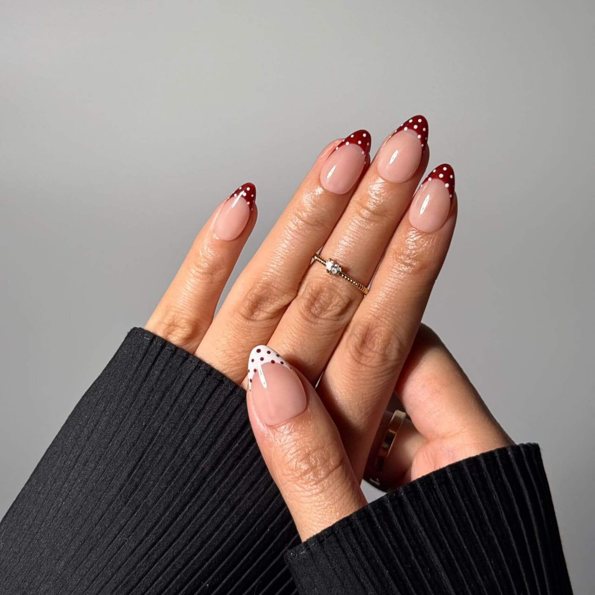 Close-up of handmade almond-shaped press-on nails showcasing the intricate red and white polka dot French tips and a high-gloss salon-quality finish.