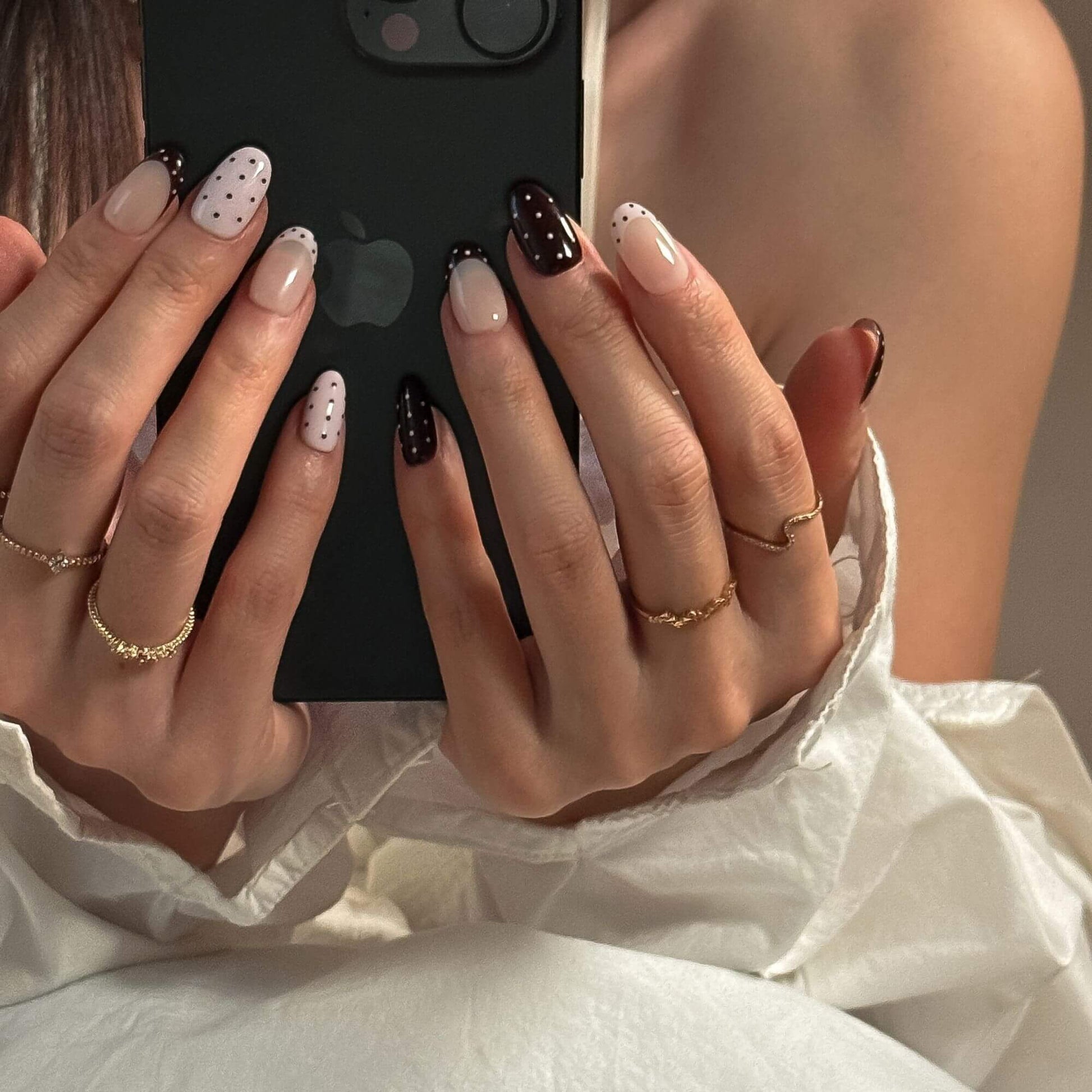 Close-up of hands holding a phone with a black case, wearing gold rings and nail polish.