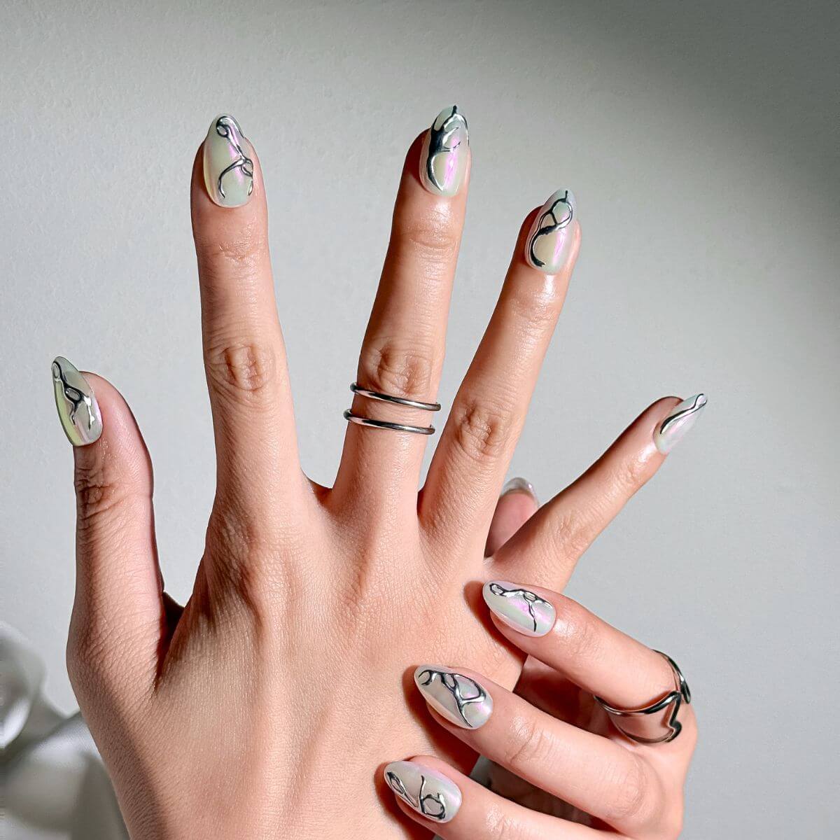 Nahaufnahme einer Hand mit mandelförmigen Press-on Nails, verziert mit 3D-Flüssigmetall-Design und passenden silbernen Ringen für einen modernen Cyber-Look.
