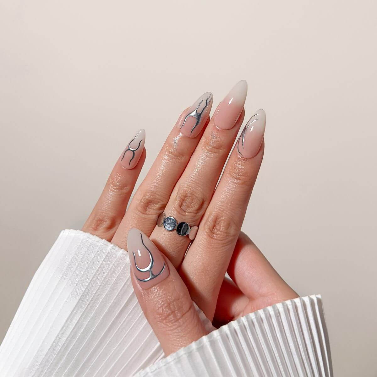 Nahaufnahme der justmee "Chrome Aura" Gel-Nägel zum Aufkleben an der Hand. Kombiniert eleganten Nude-Farbverlauf mit futuristischen silbernen Chrome-Akzenten.