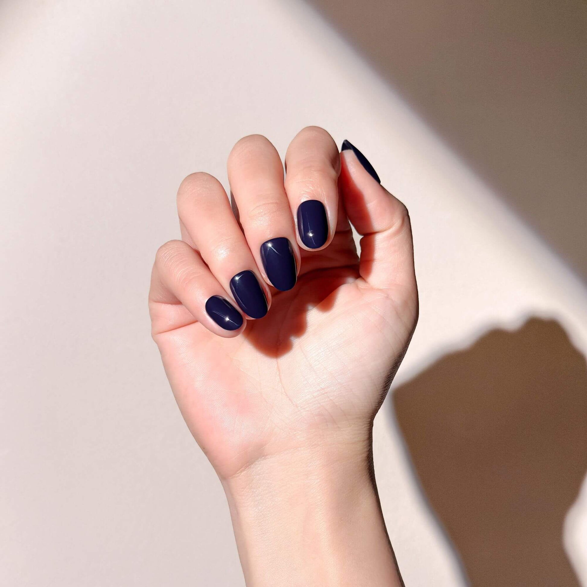 A hand wearing elegant short oval navy blue nails with a high-gloss finish.