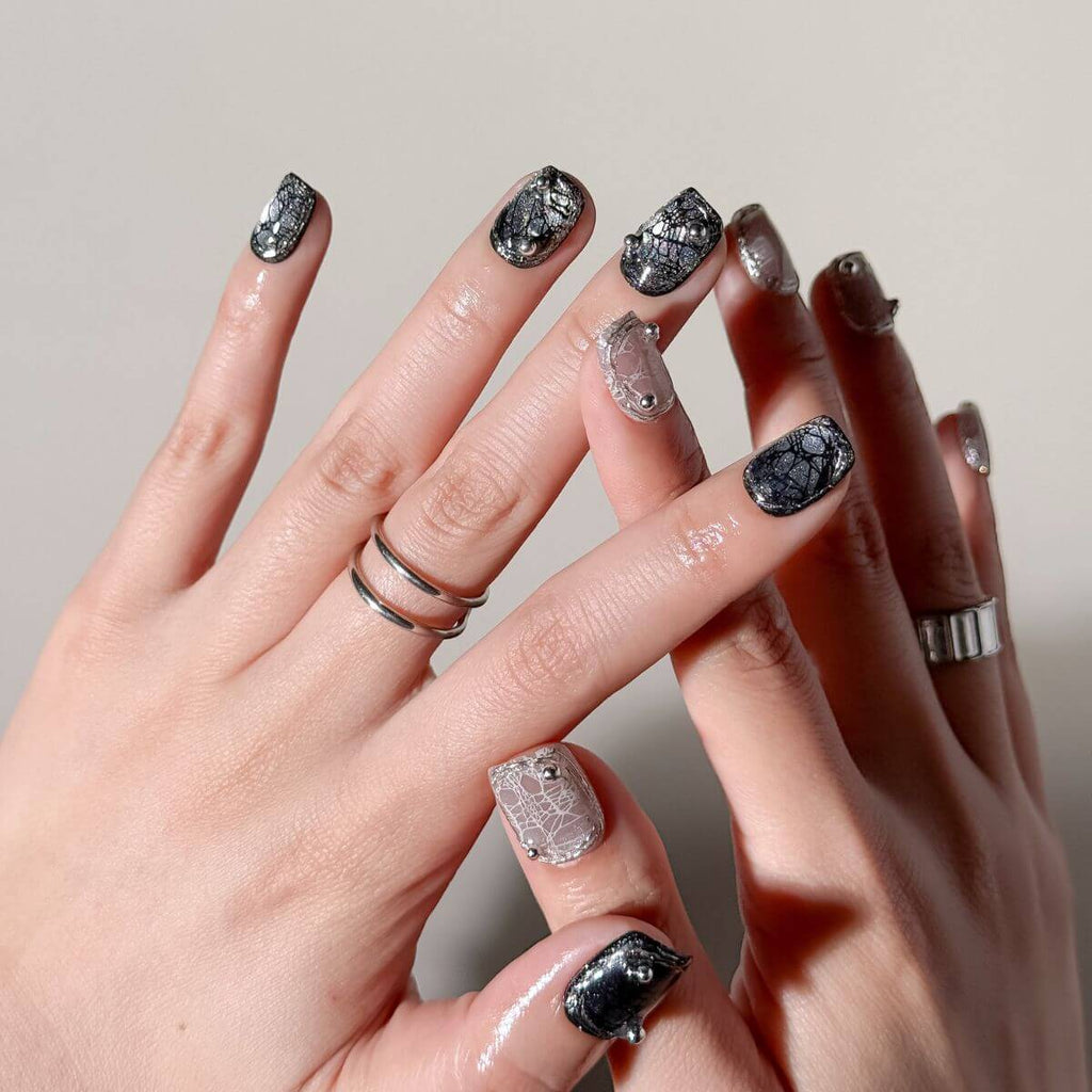 Close-up of hands with 10 press-on nails featuring black and nude spider web crackle designs with 3D silver beads
