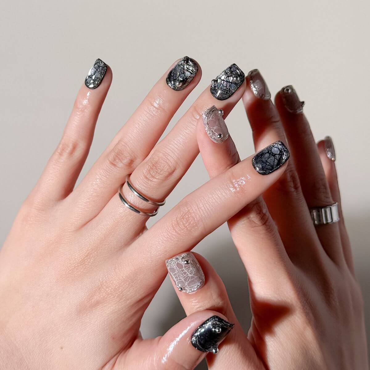 Close-up of hands with 10 press-on nails featuring black and nude spider web crackle designs with 3D silver beads