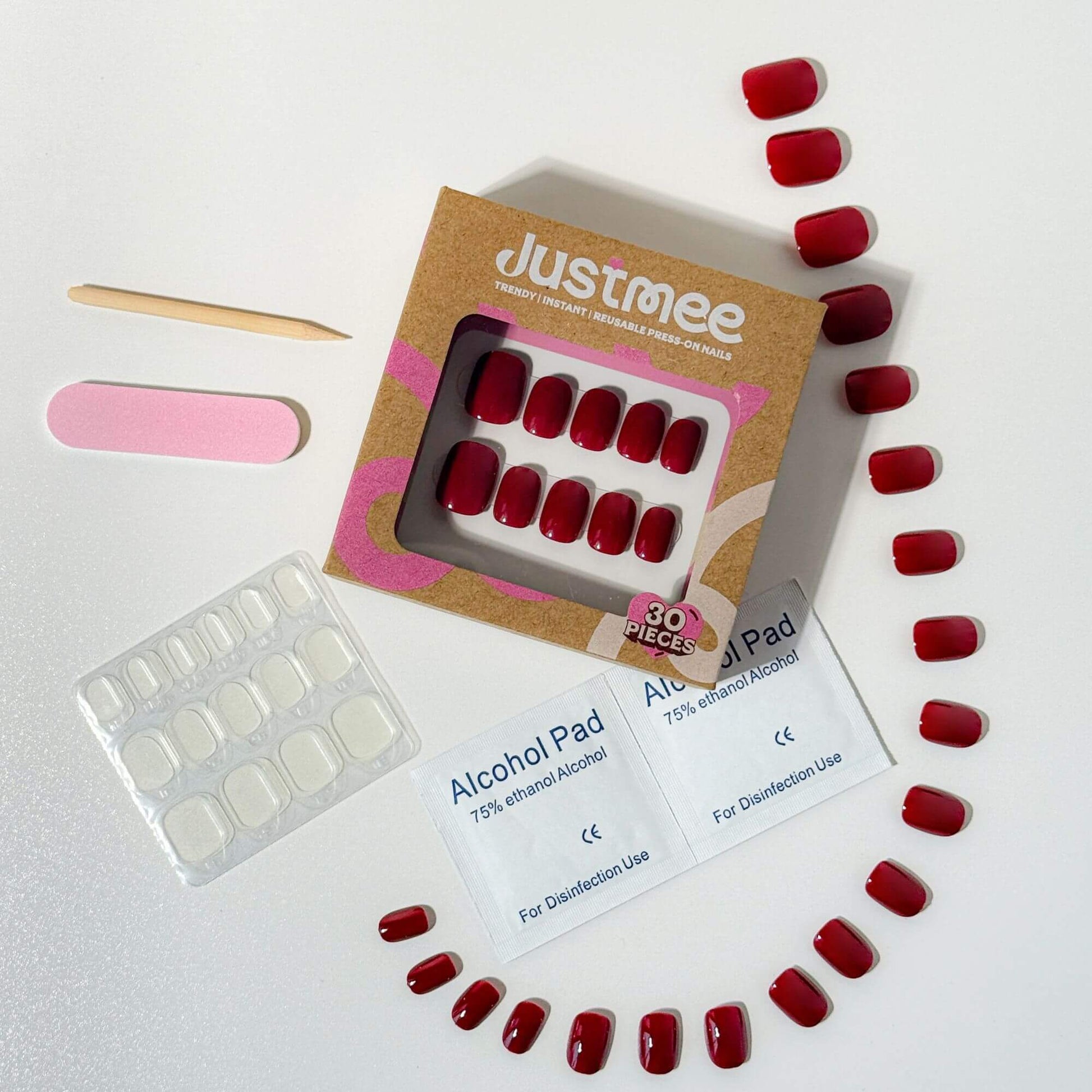 Top-down view of the Justmee cherry red press-on nail kit featuring 30 nails, adhesive tabs, prep pads, and a nail file for a professional home manicure.