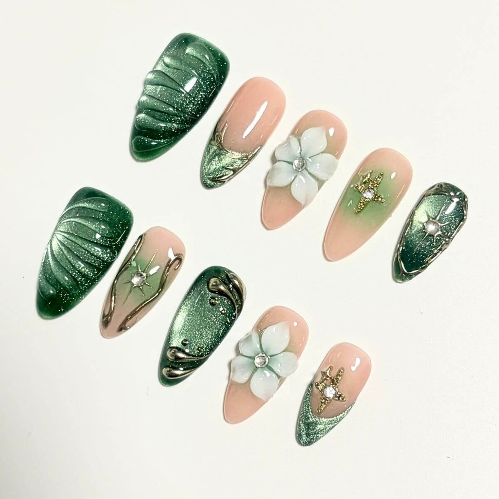 A complete product overview flat lay of the Emerald Eden artificial nail set, showing 10 stylized sample nails with 3D star charms, textured green shells, and porcelain flowers.