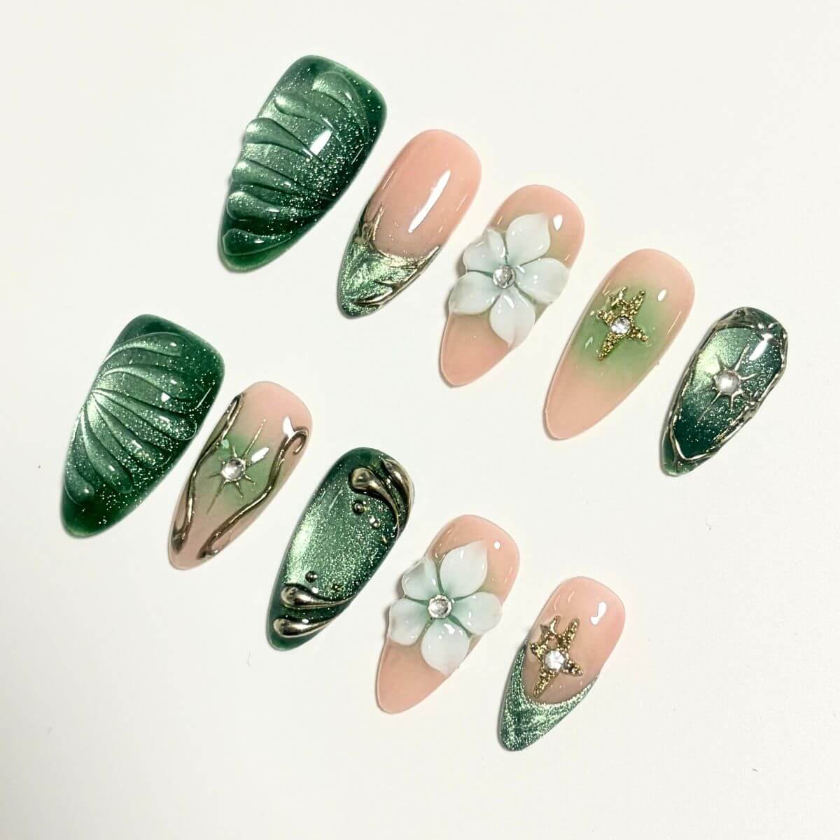 A complete product overview flat lay of the Emerald Eden artificial nail set, showing 10 stylized sample nails with 3D star charms, textured green shells, and porcelain flowers.