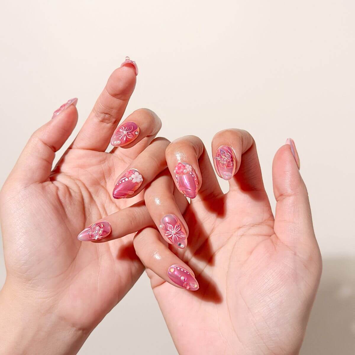 Lifestyle-Foto von zwei ineinandergelegten Händen mit künstlichen Fingernägeln in Pink-Metallic, kunstvollen 3D-Schmetterlingen und schimmernden Chrome-Effekten.