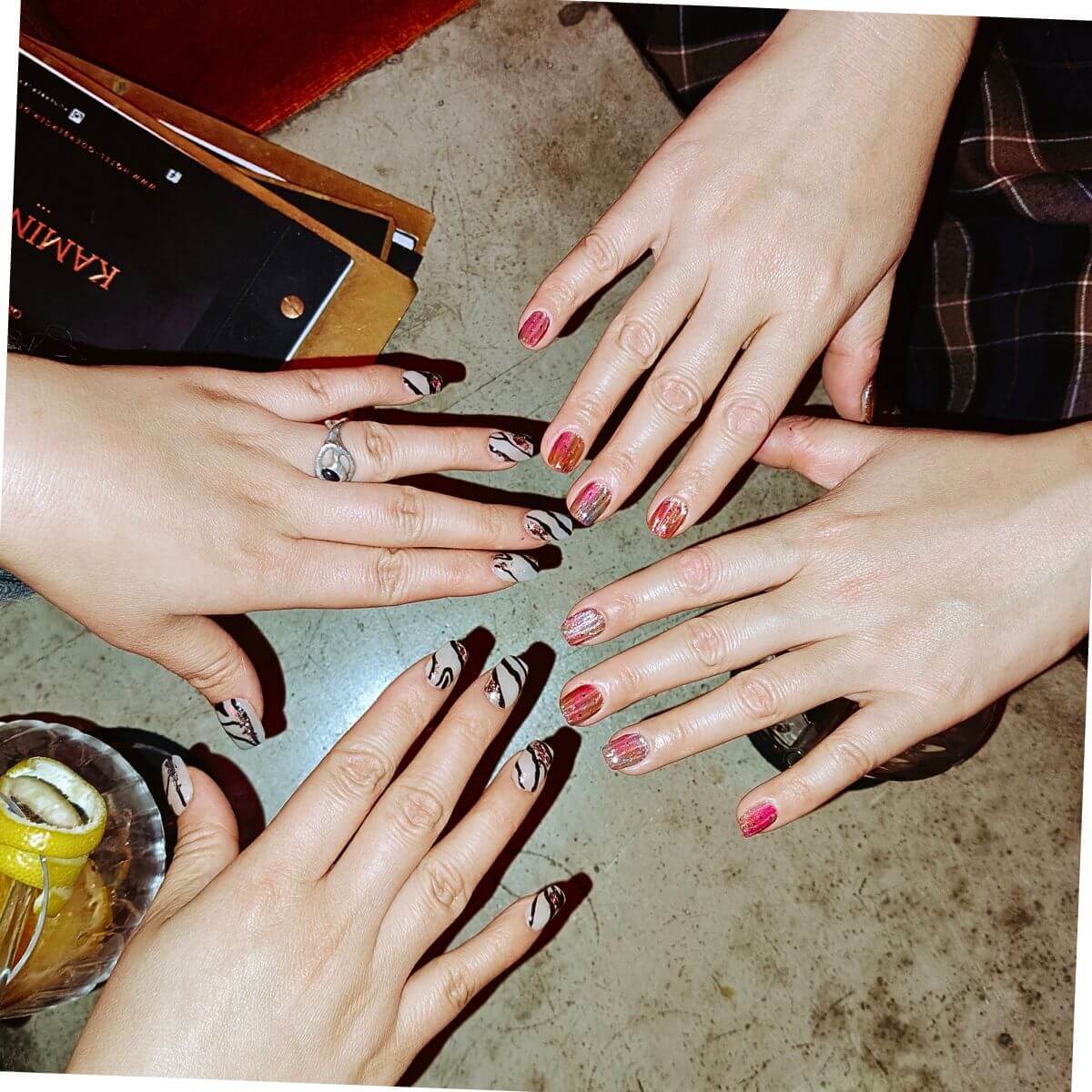 Gruppenaufnahme von vier Händen, die verschiedene Nageldesigns zeigen, darunter funkelnder Roségold-Glitzer, French Tips im Zebra-Look und minimalistische schwarze Linien.