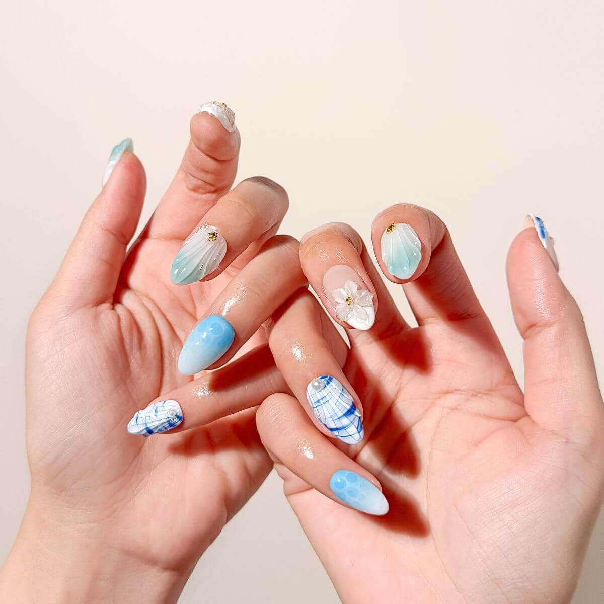 Lifestyle-Foto von zwei Händen mit mintgrünen und blauen Kunstnägeln in Mandelform, verziert mit 3D-Wasser-Effekten und feinen Perlen.