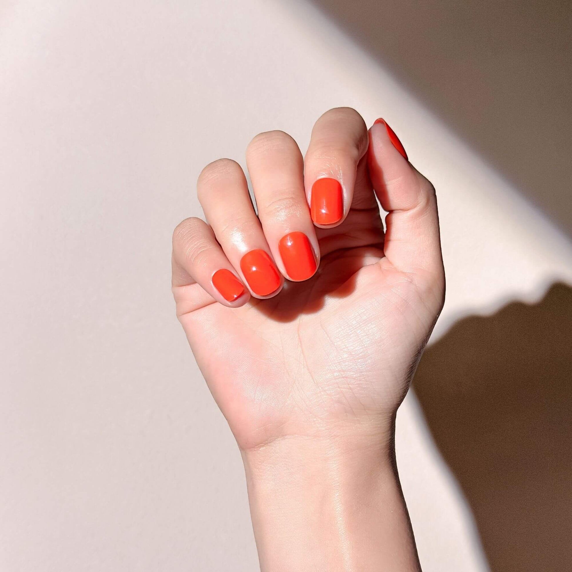 Close-up of a hand model wearing glossy bright orange short press-on nails.