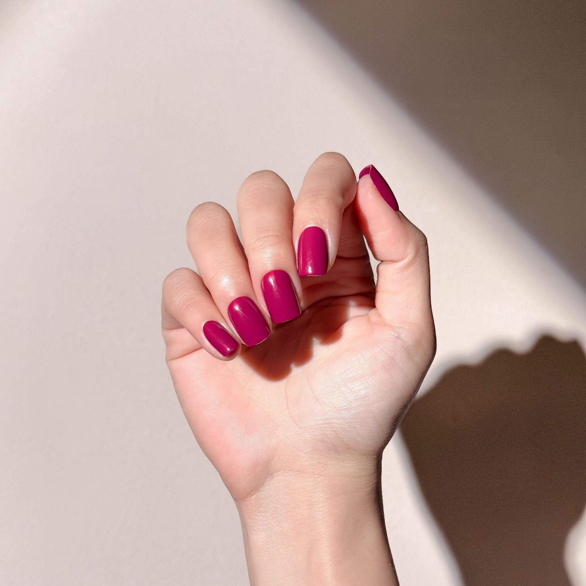 Handmodell mit kurzen quadratischen Press-on-Nägeln in Magenta-Beere für einen natürlichen und eleganten Maniküre-Look.