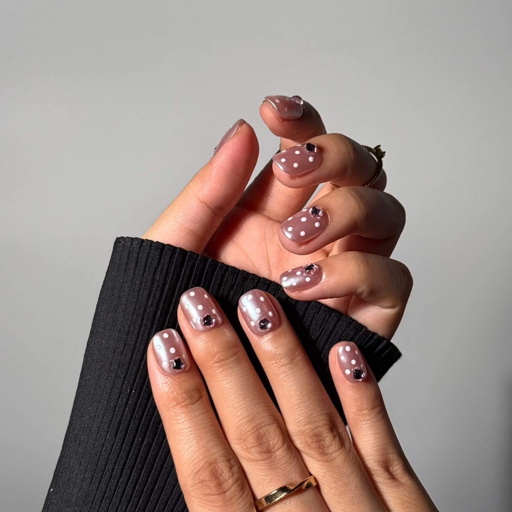 Close-up of handmade short square nails showcasing the reflective mauve chrome finish, crisp white polka dots, and secure 3D rhinestone placement.