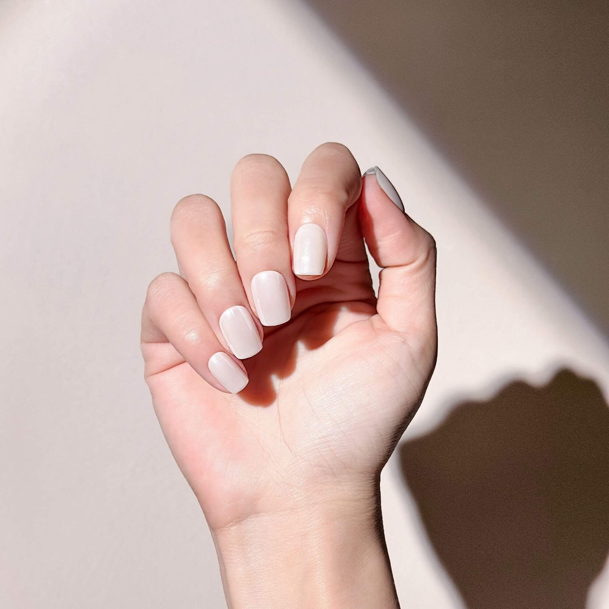 Handmodell mit eleganten milchweißen Nägeln in kurzer, eckiger Form.