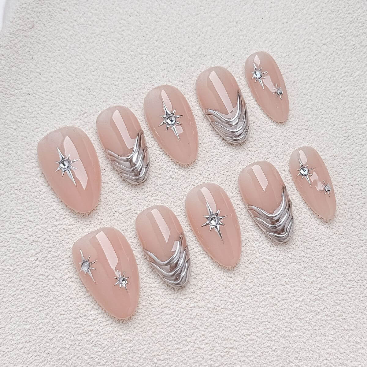 Draufsicht auf ein Set künstlicher Press-On Nägel in mittellanger Mandelform mit hochglänzender Nude-Rosa-Basis, verziert mit metallischen silbernen 3D-Chromwellen und minimalistischen Sternen-Details.