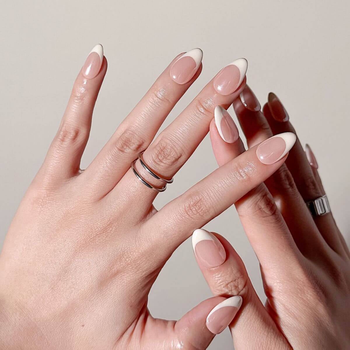 Close-up of a flawless salon-quality DIY manicure showing hands with almond press-on nails in classic French style with chrome undertones.