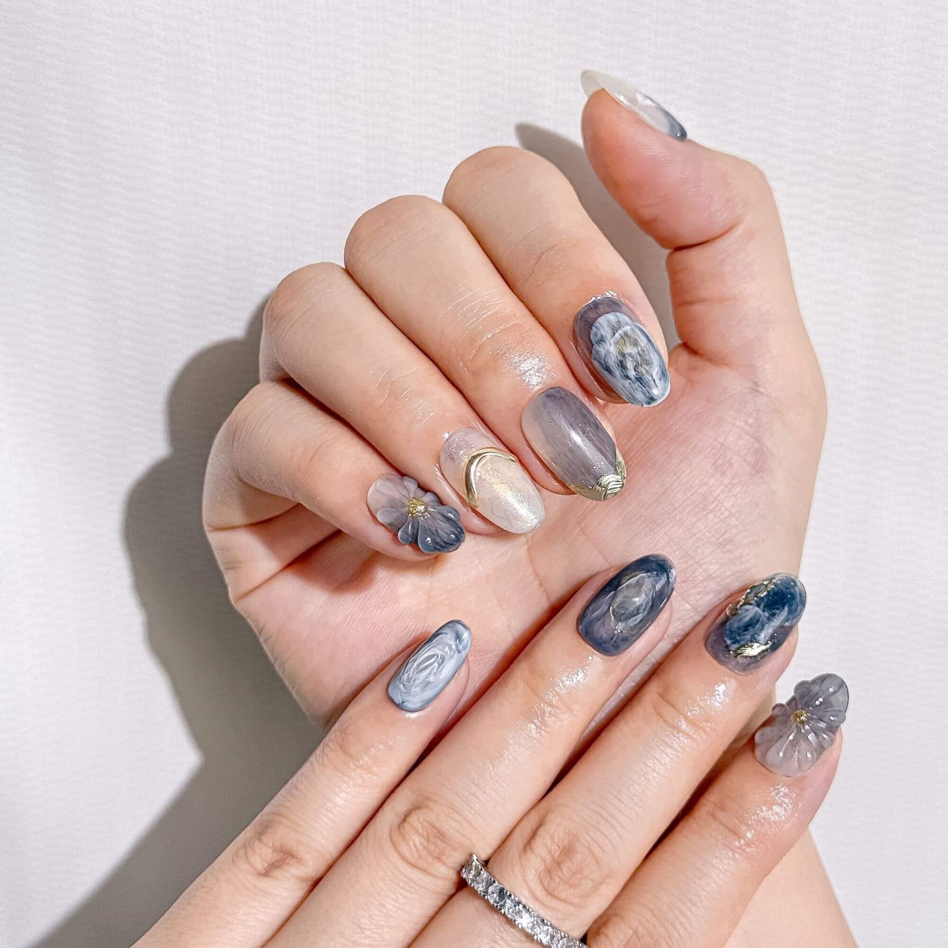 Detailaufnahme der Blue Mirage Press-on-Nägel, die die einzigartigen handgefertigten Gold-Akzente und die Tiefe des floralen Marmor-Finishs zeigt.