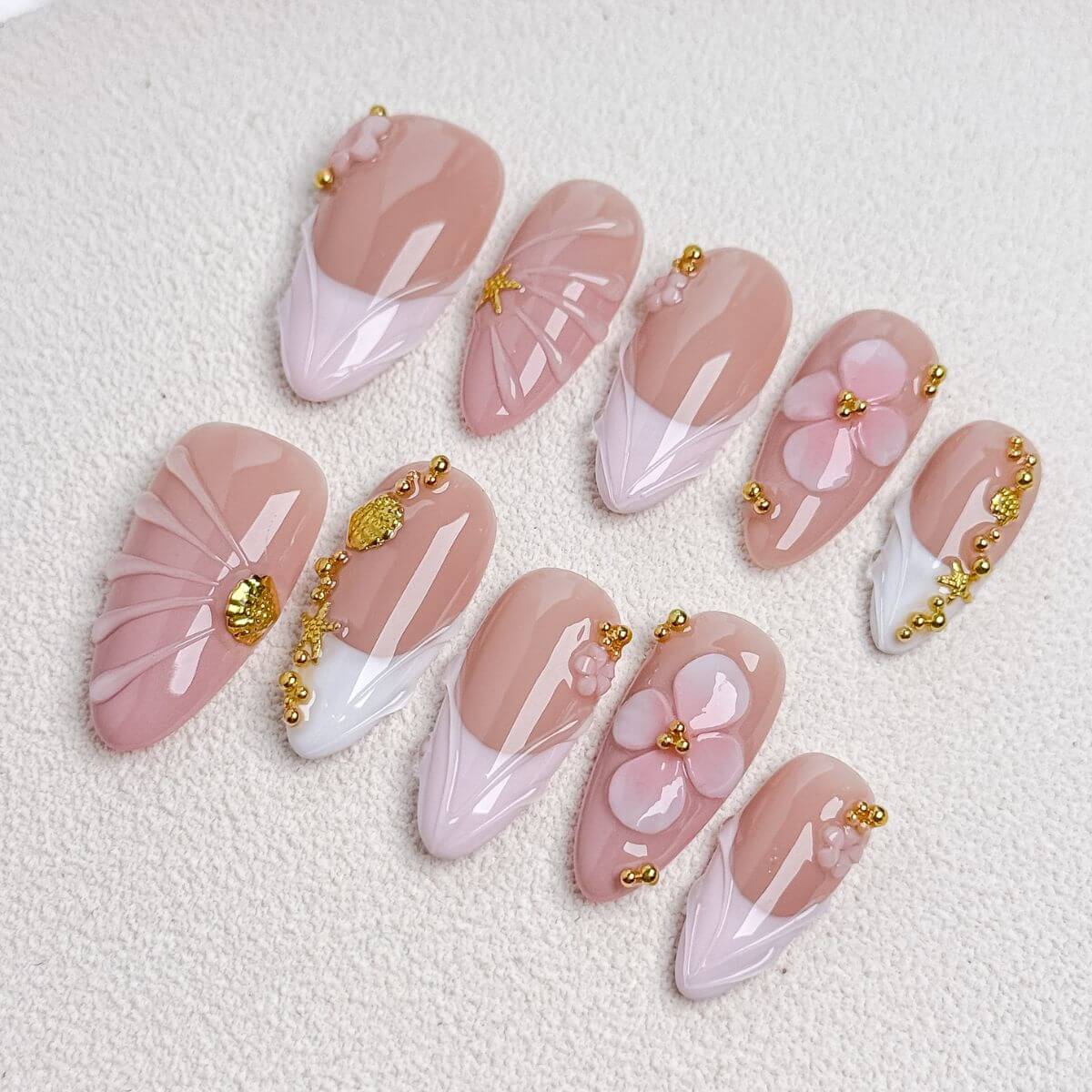 Eine Produktübersicht des Blush Ballet Sets mit künstlichen Nägeln, die pastellrosa V-French-Tips, 3D-Blüten, Muschel-Strukturen und goldene Perlen zeigt.