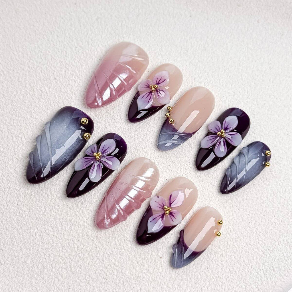 Eine flache Produktübersicht des Amethyst Velvet Sets mit künstlichen Nägeln, die detailliert violette 3D-Blüten, grauen Cat-Eye-Schimmer und altrosa Reliefs zeigt.