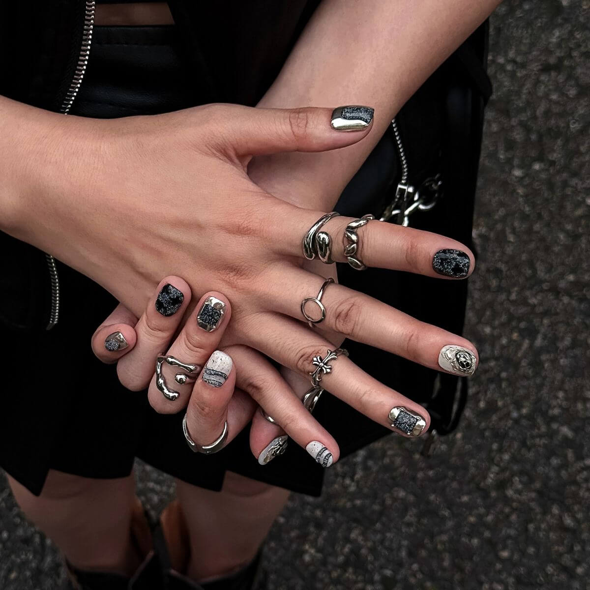Nahaufnahme von Händen mit kurzen, eckigen Press-On Nails in einer Mischung aus strukturiertem schwarzem Glitzer, flüssigem Silber-Metallic und abstrakten Linien.