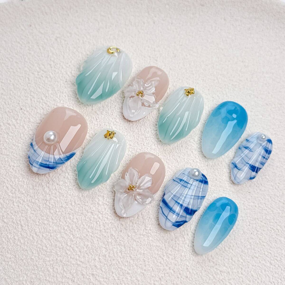 Eine Produktübersicht des Pacific Breeze Sets mit künstlichen Nägeln, die türkis-mintgrüne Farbverläufe, Wassertropfen-Strukturen, transparente Blüten und Karo-Muster zeigt.