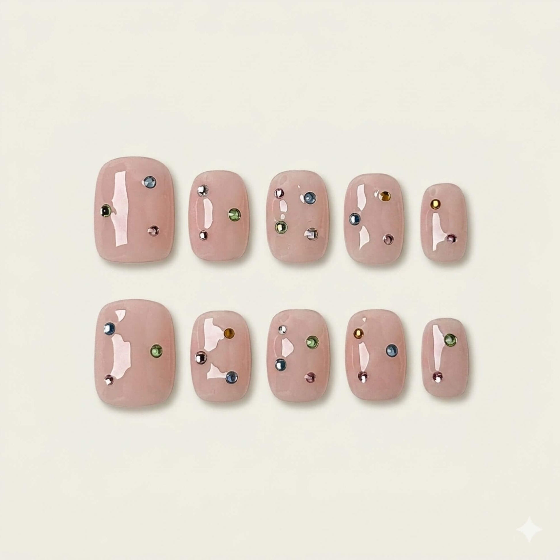 A flat lay display of 10 handmade short square press-on nails from the Prism Petal collection, featuring a sheer nude pink base and delicate multi-colored rhinestone accents.
