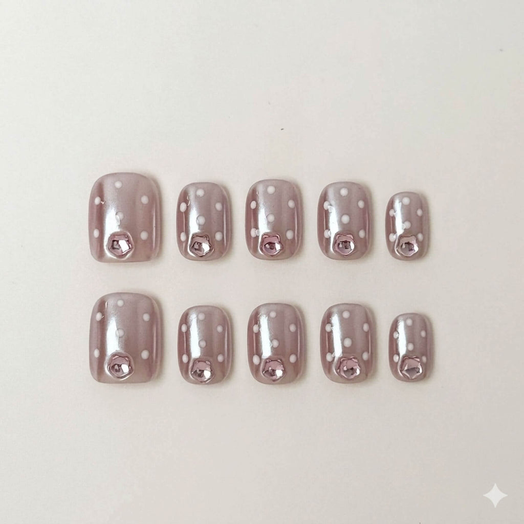 Eine Produktübersicht von 10 handgefertigten kurzen eckigen Press-on-Nägeln mit mauvefarbener Chrome-Basis, weißen Punkten und rosa Schmuckstein-Akzenten.