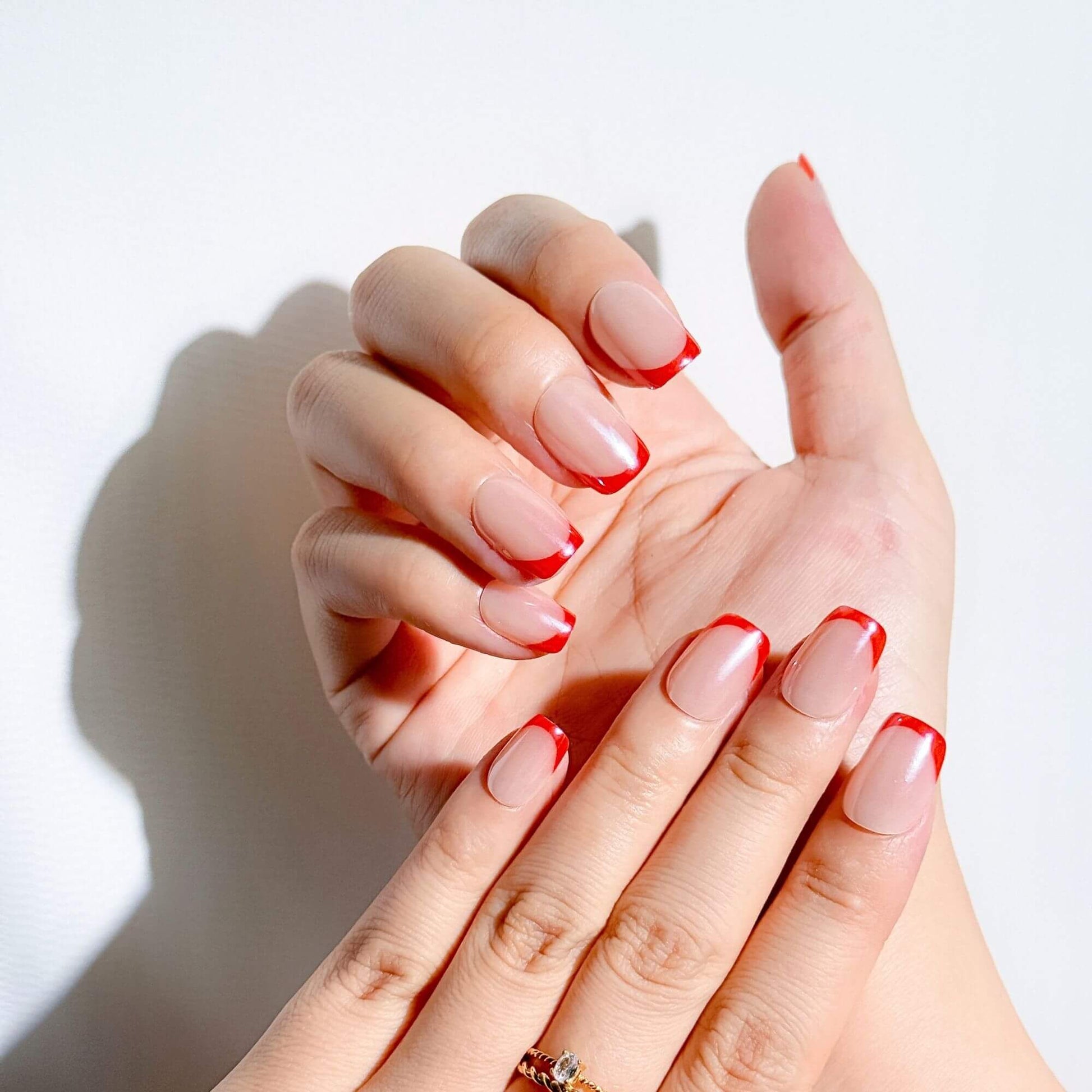 Hände mit Justmee kurzen Press-on-Nägeln mit roten French Tips, die eine elegante und mutige Variante der klassischen French Manicure mit natürlicher Passform zeigen.
