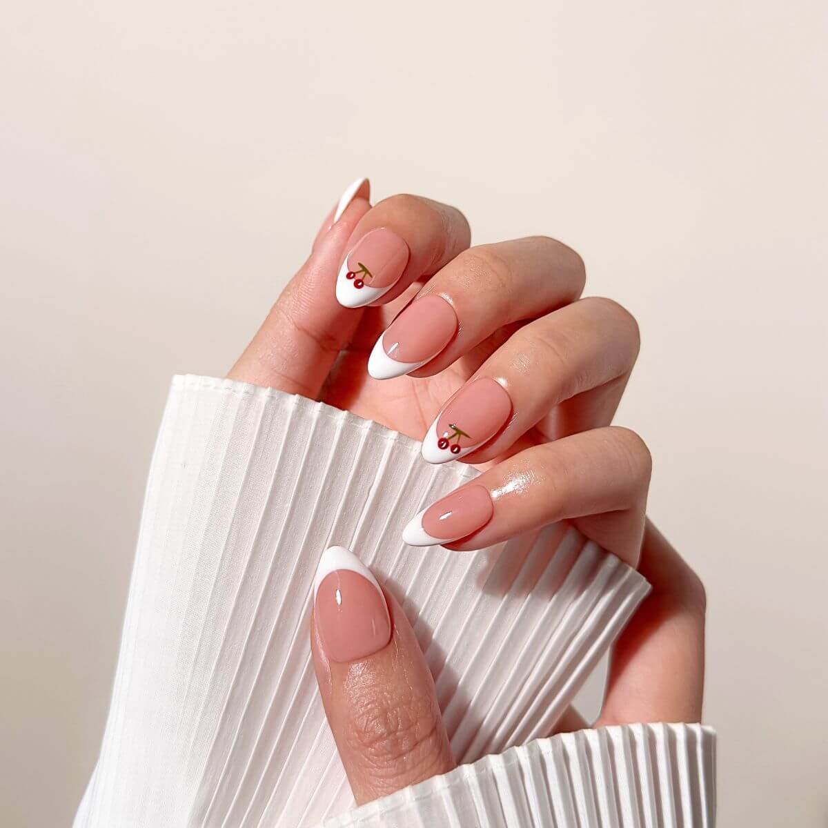 Model hand resting on a white pleated sleeve displaying the Cherry Classic manicure, highlighting the clean girl aesthetic and glossy round silhouette.