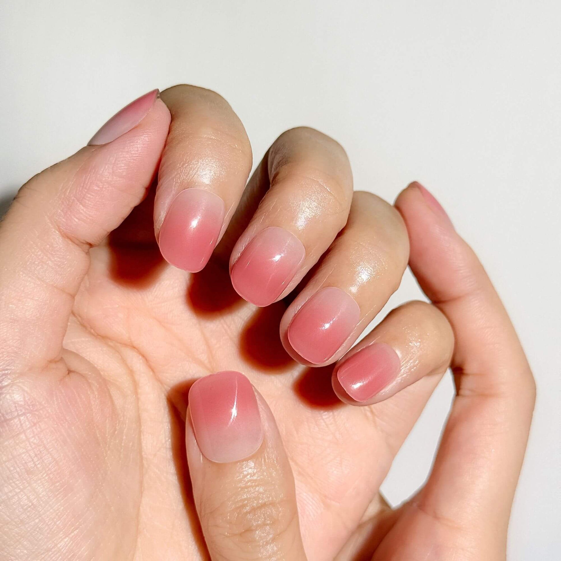 A hand wearing Justmee rose pink ombre press-on nails in a short length, showing a natural and seamless fit at the cuticles with a healthy glow.