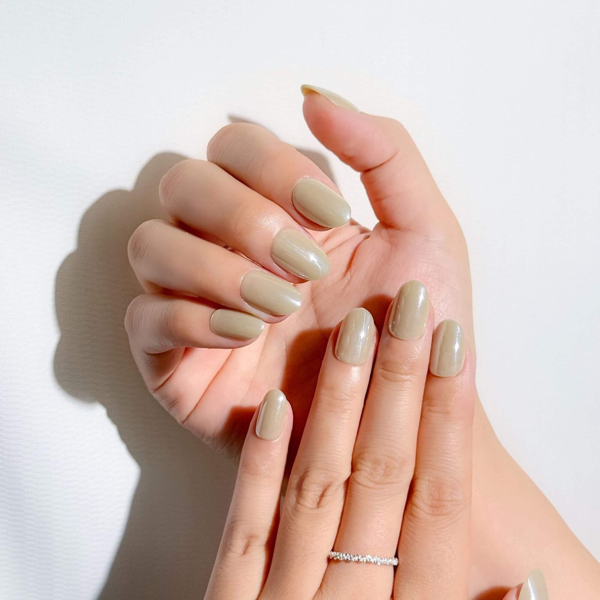 Hands wearing Justmee sage green oval press-on nails, demonstrating a natural, earthy manicure style.