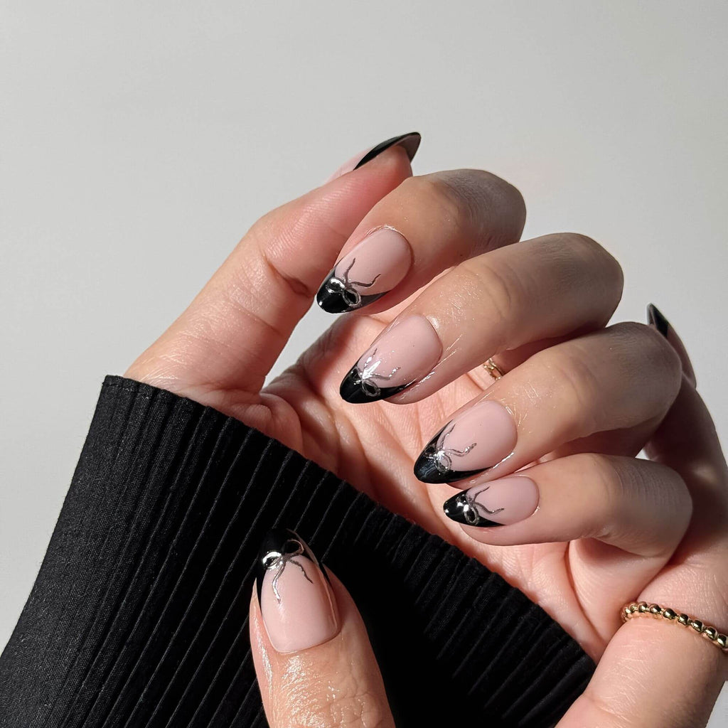 Close-up view of elegant black French tip press-on nails with silver chrome bow accents in natural lighting.