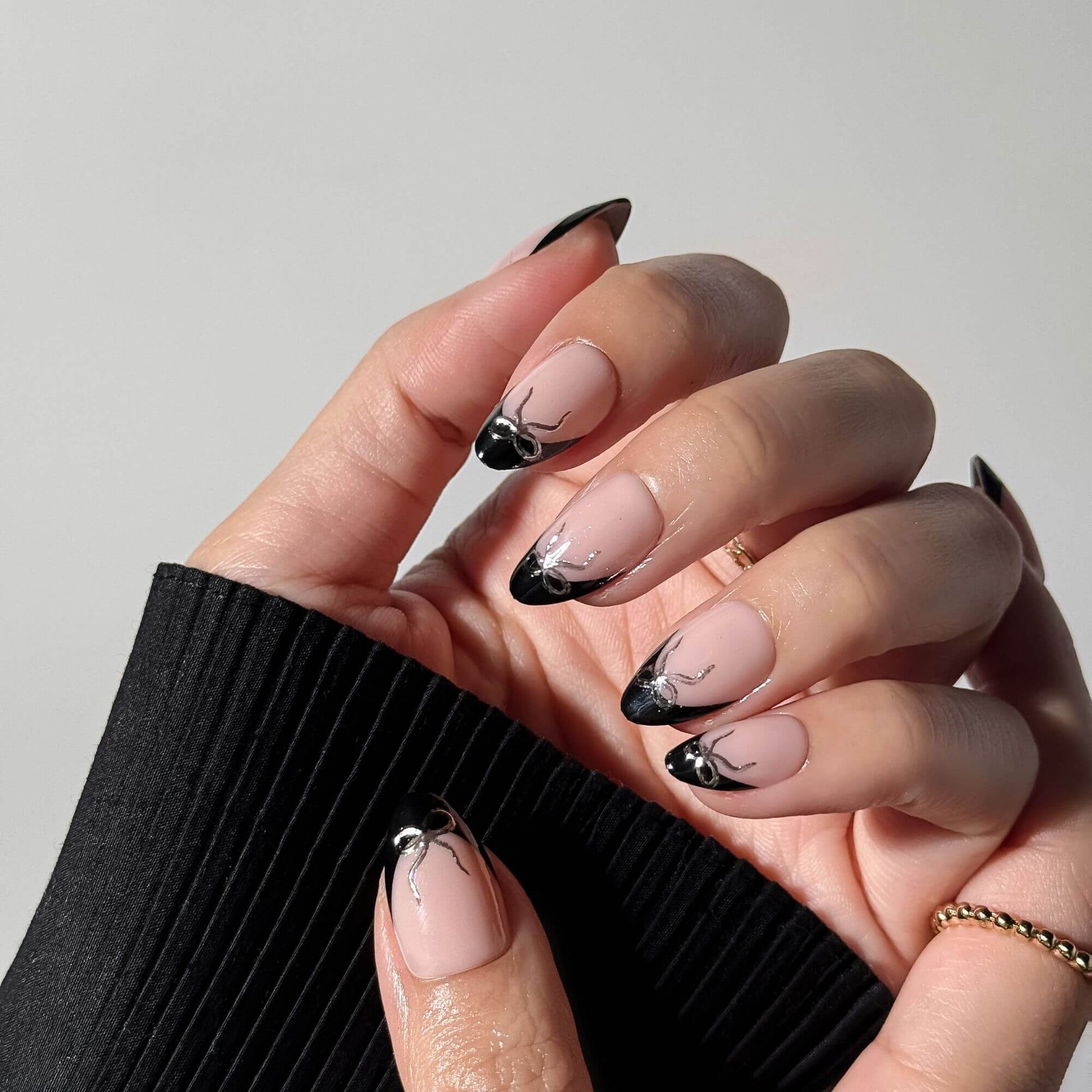 Close-up view of elegant black French tip press-on nails with silver chrome bow accents in natural lighting.