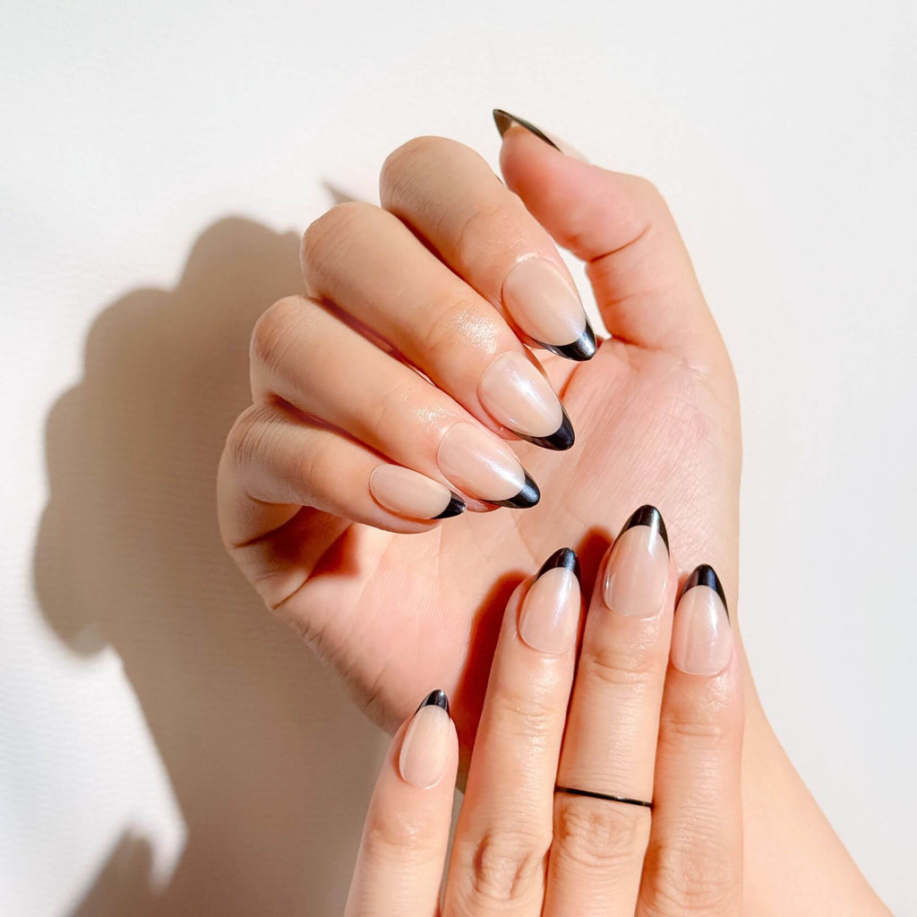 Lifestyle shot of a hand wearing Justmee black French tip almond nails, showing how the medium length and shape create an elongated, salon-quality look.
