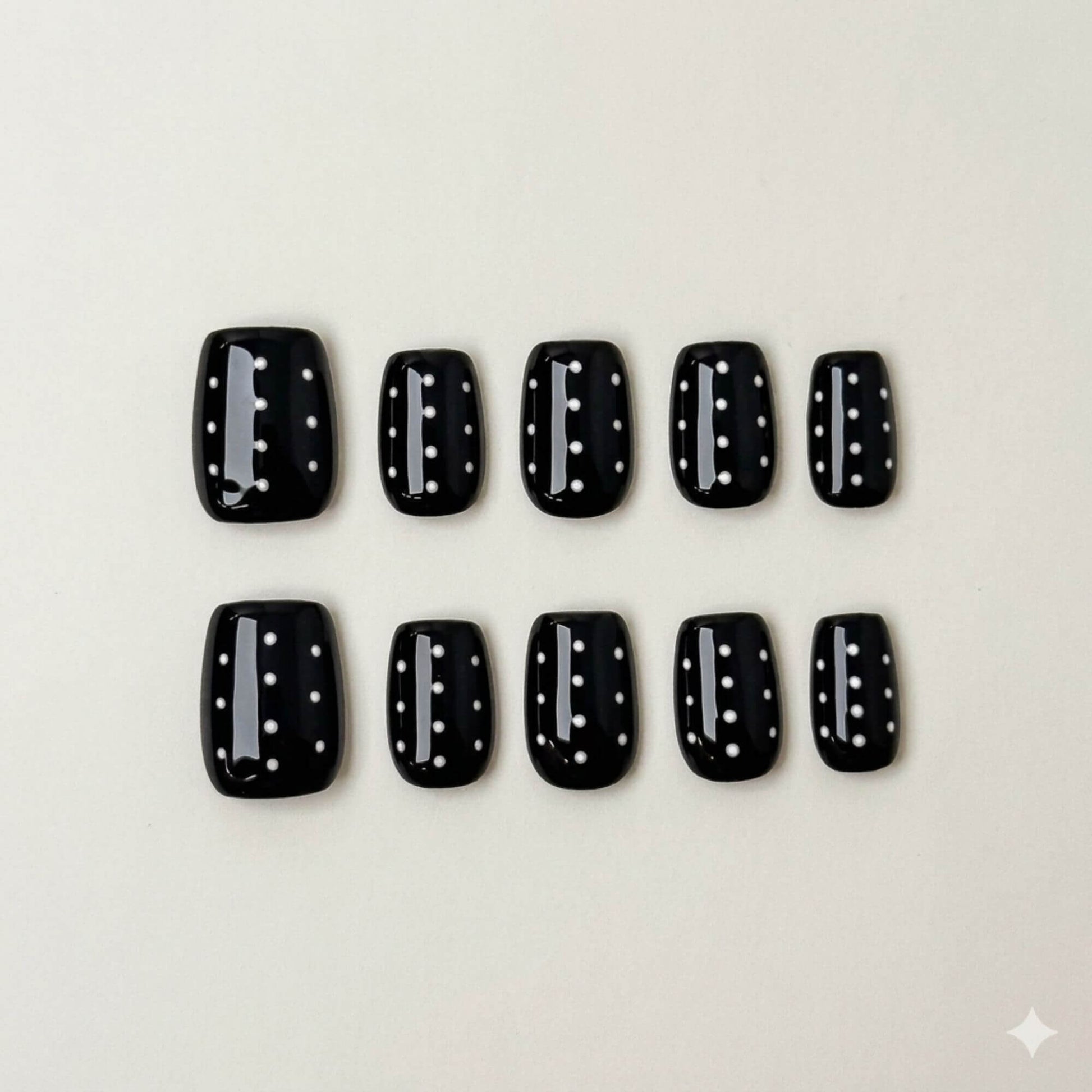 Eine Produktübersicht von 10 handgefertigten kurzen eckigen Press-on-Nägeln mit einer glänzenden schwarzen Basis und weißen Punkten.