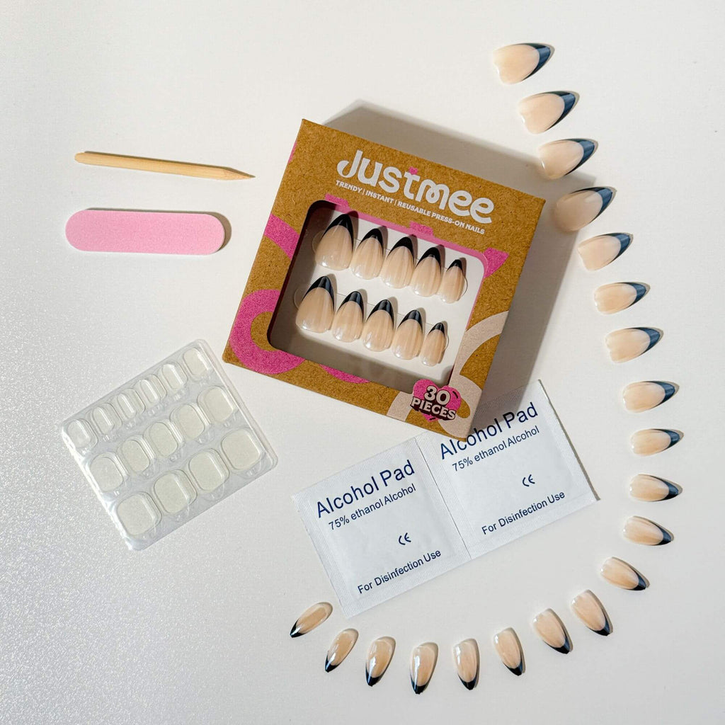A complete Justmee almond-shaped press-on nail kit featuring black French tips on a nude base, including adhesive tabs, nail file, and prep tools.