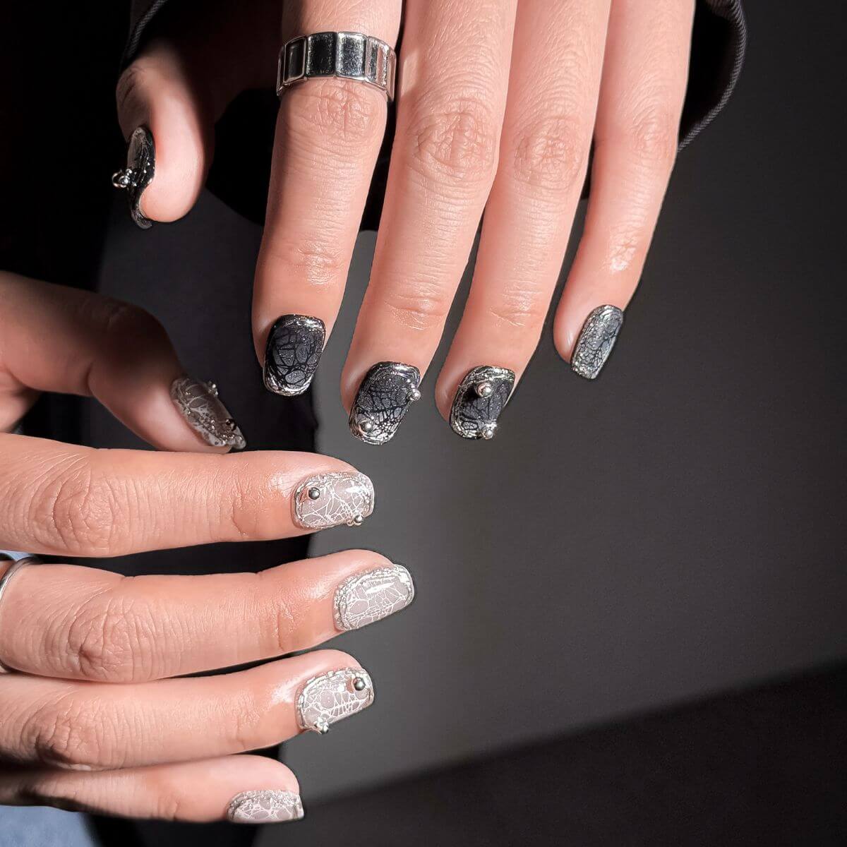 Close-up of hands with press-on nails of gothic spider web design in square shape on a dark background